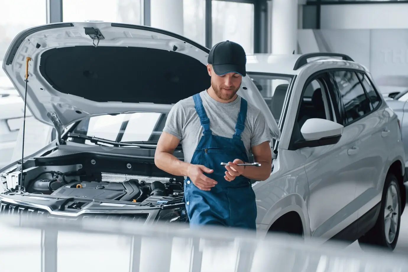 Taking a break at work, an employee in a blue uniform stands in a car showroom.